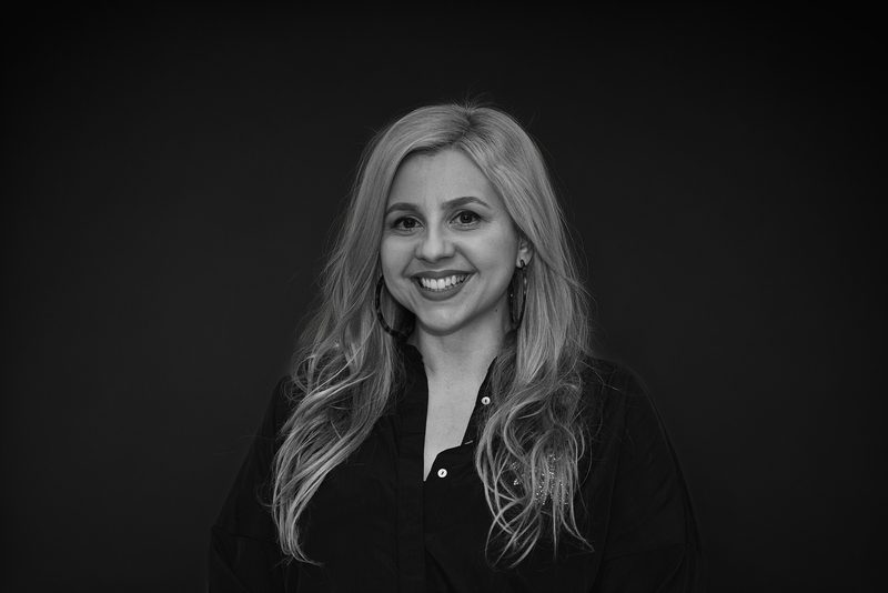Black and white headshot of a smiling woman with long wavy blonde hair